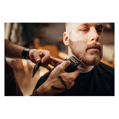 Fotografie Male barber cutting beard of client in barber shop, South_agency